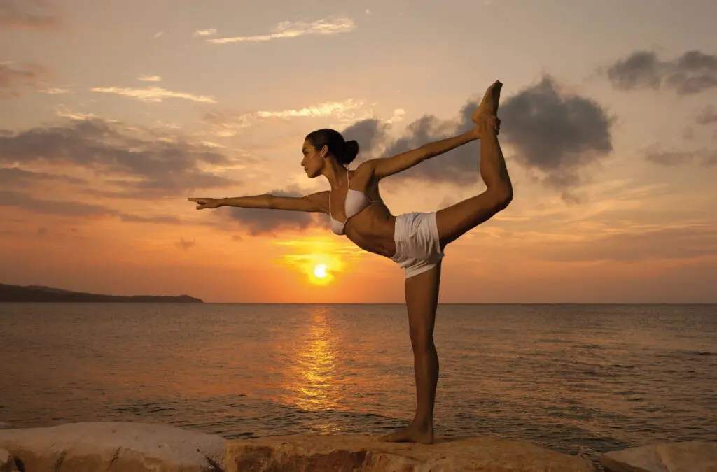 Woman doing yoga at sunset on rocks by the ocean